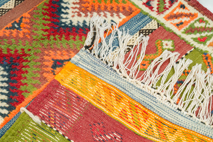 Close-up of a colorful woven rug with geometric patterns and white fringe tassels.