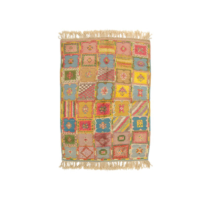 A rectangular patchwork-style moroccan rug with fringed top and bottom edges, featuring a multicolor grid of geometric and floral motifs in pink, yellow, blue, green, and beige tones on a white background.