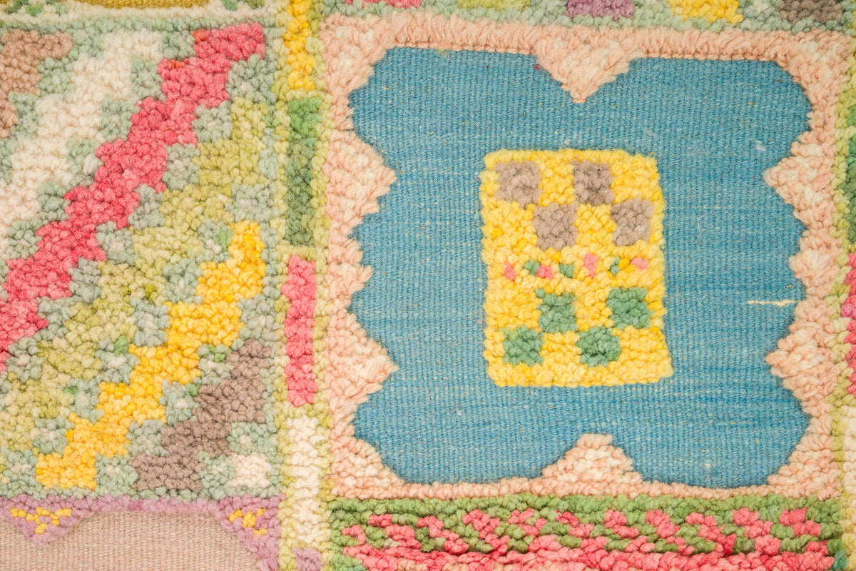 Close-up of a colorful hand-knotted hand woven moroccan rug showing a blue central motif with a yellow floral center, surrounded by pink, green, and beige textured sections.