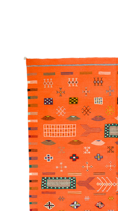 An orange Moroccan rug with a colorful geometric pattern, shown against a plain white background.