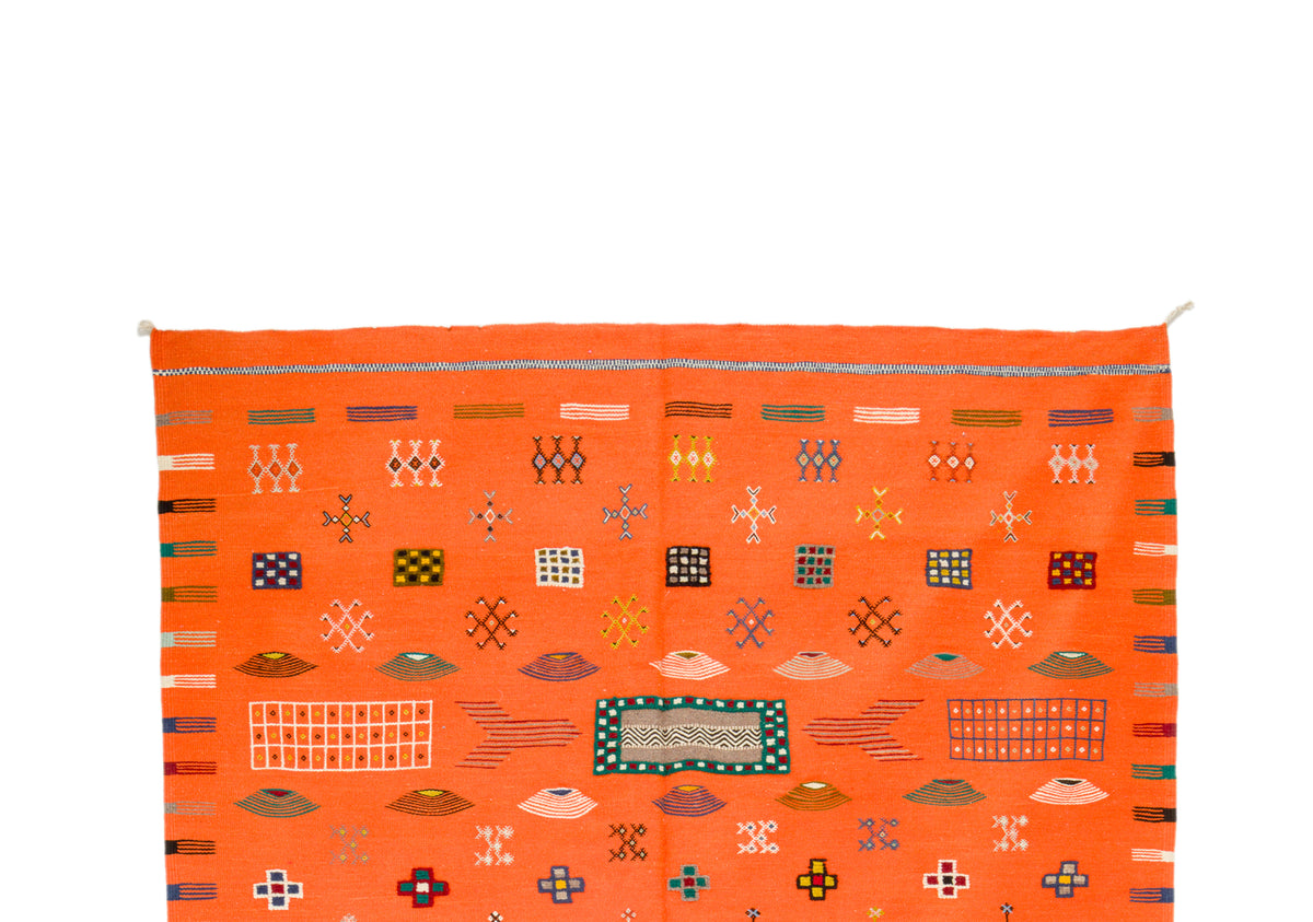 An orange Moroccan woven rug with geometric patterns and colorful accents, shown against a plain white background.