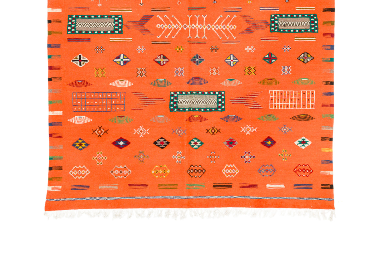 An orange Moroccan wool rug with geometric patterns and white fringe at the bottom, shown flat against a white background.