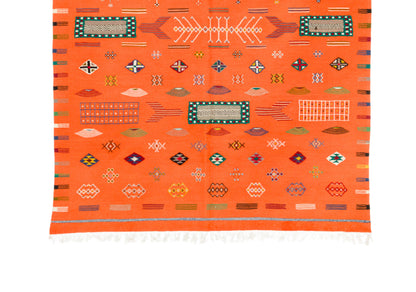 An orange Moroccan wool rug with geometric patterns and white fringe at the bottom, shown flat against a white background.
