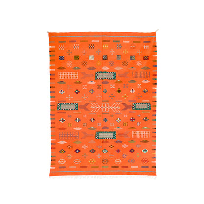 An orange Moroccan woven rug with a geometric pattern, featuring a central fish motif, diamond shapes, and striped borders on a white background.