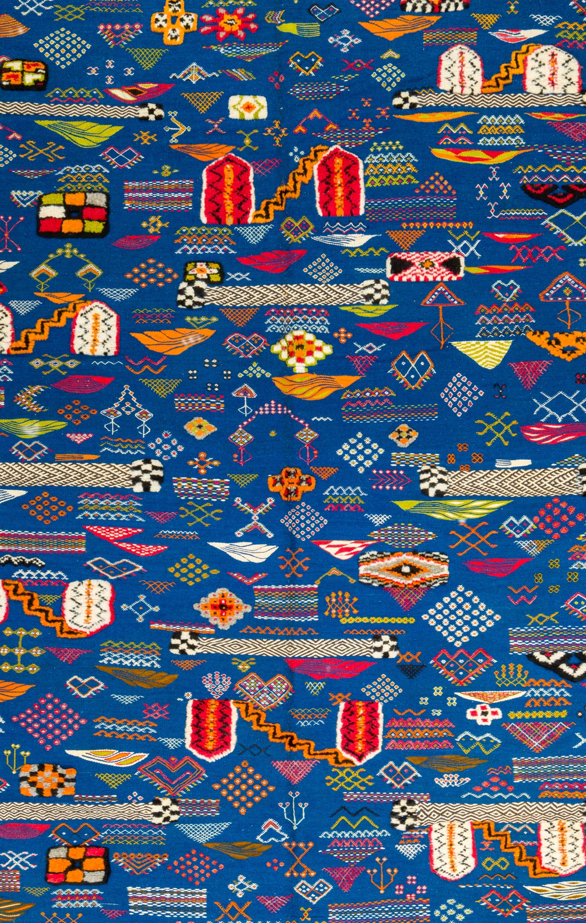 A close-up of a Moroccan blue rug featuring an all-over multicolor geometric and tribal-inspired pattern with red, yellow, white, black, and orange motifs.