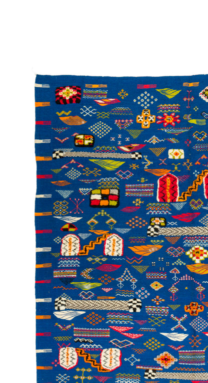 A close-up of a blue Moroccan kilim wool rug featuring intricate multicolor geometric patterns and traditional motifs.