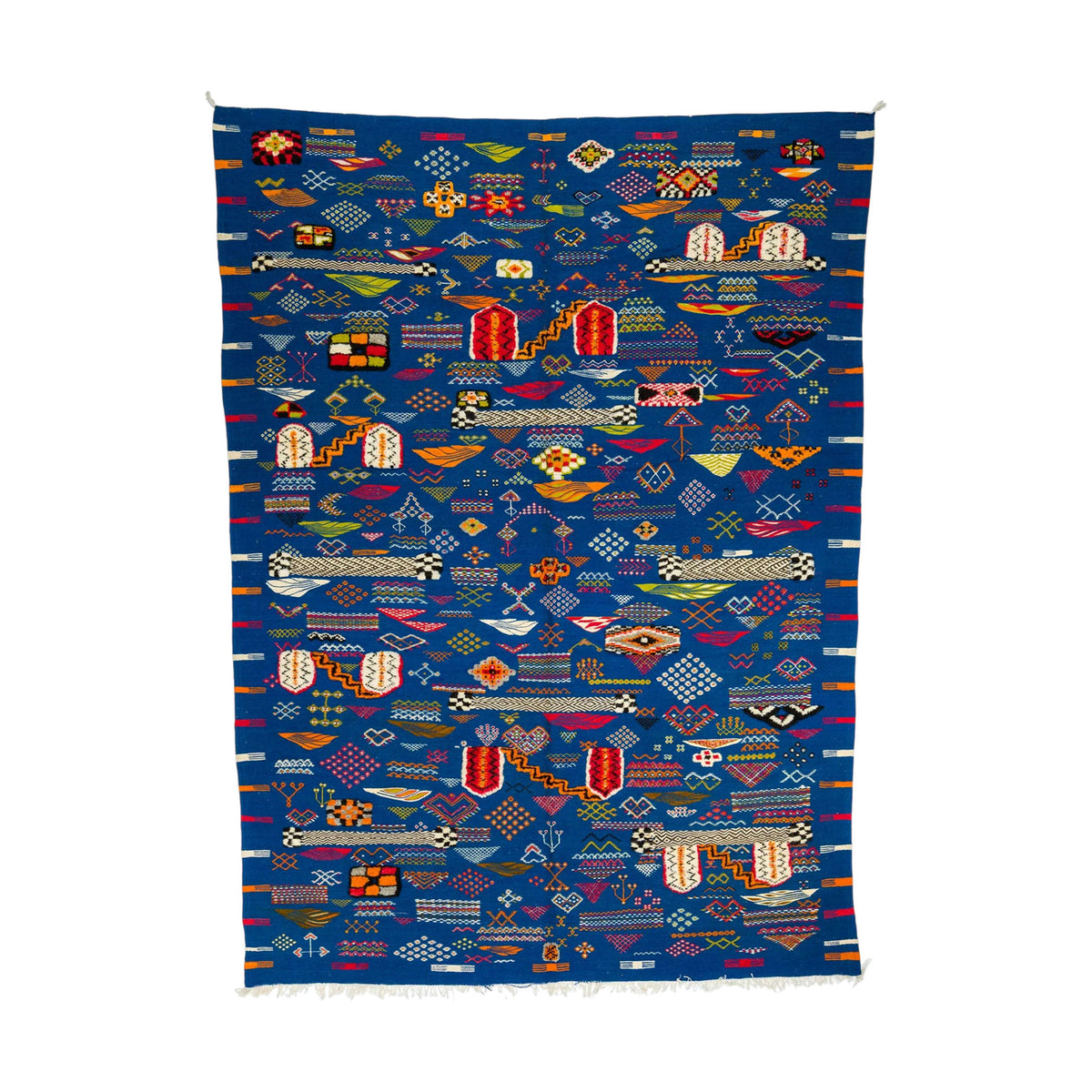 A square blue Moroccan woven rug with a dense, colorful geometric patterns, flags, and abstract shapes, finished with white fringe on the bottom edge.