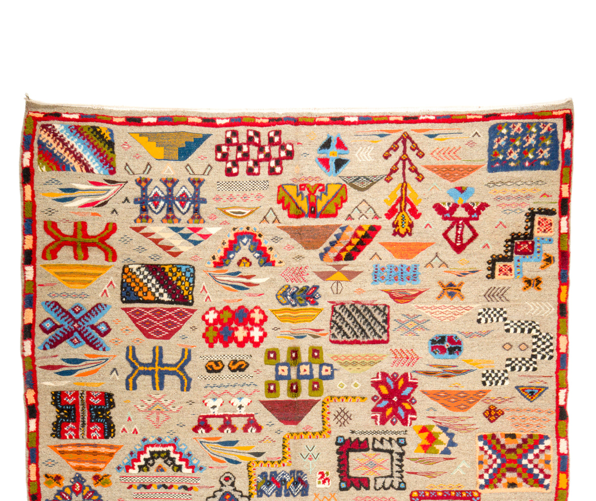 A square handwoven rug with a cream-colored base and a dense, colorful geometric pattern of tribal motifs, including diamonds, triangles, and abstract symbols in red, blue, yellow, green, and black.