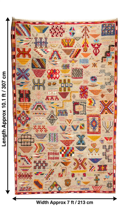 A flat-lay view of a large Moroccan wool rug with dimensions annotated on the left and bottom. The rug features a cream-colored base with a dense, multicolored patchwork of geometric and tribal patterns including red, blue, yellow, green, and black.