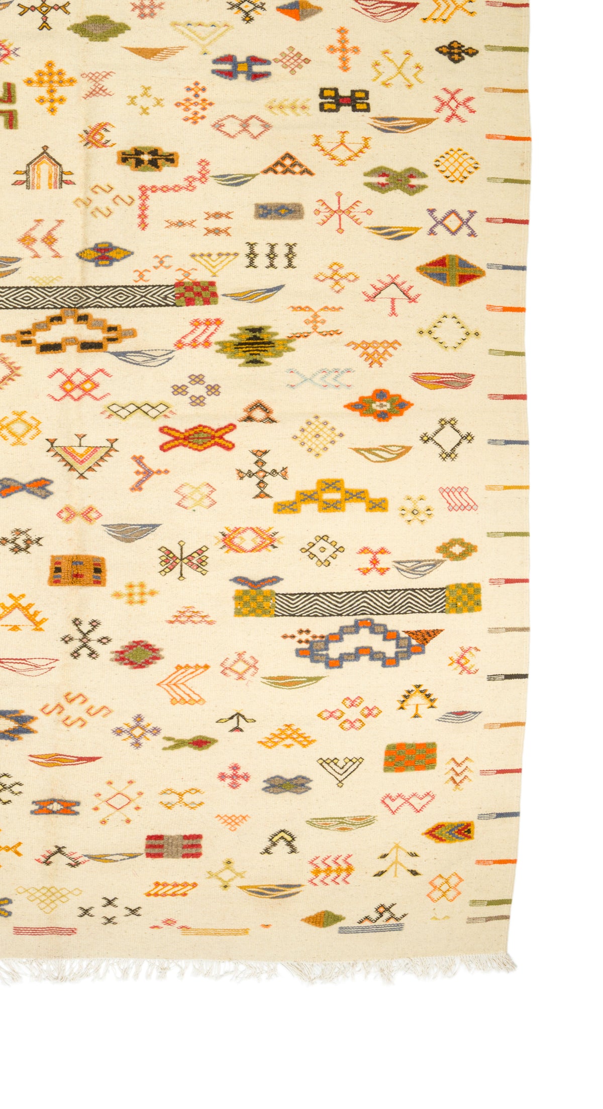 A close-up of a wovenwool rug with a cream background and dense multicolor geometric and tribal-style motifs, including orange, red, yellow, green, and brown elements, with fringe visible along the bottom edge.