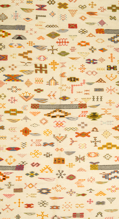 A close-up of a Moroccan with a dense, repeating geometric pattern in orange, brown, olive green, and red on a warm cream background.