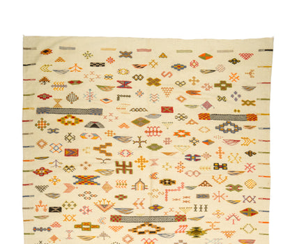 A Moroccan Kilim wool rug with an off-white base and dense geometric patterns in orange, brown, olive green, gray, and black, photographed flat against a white background.