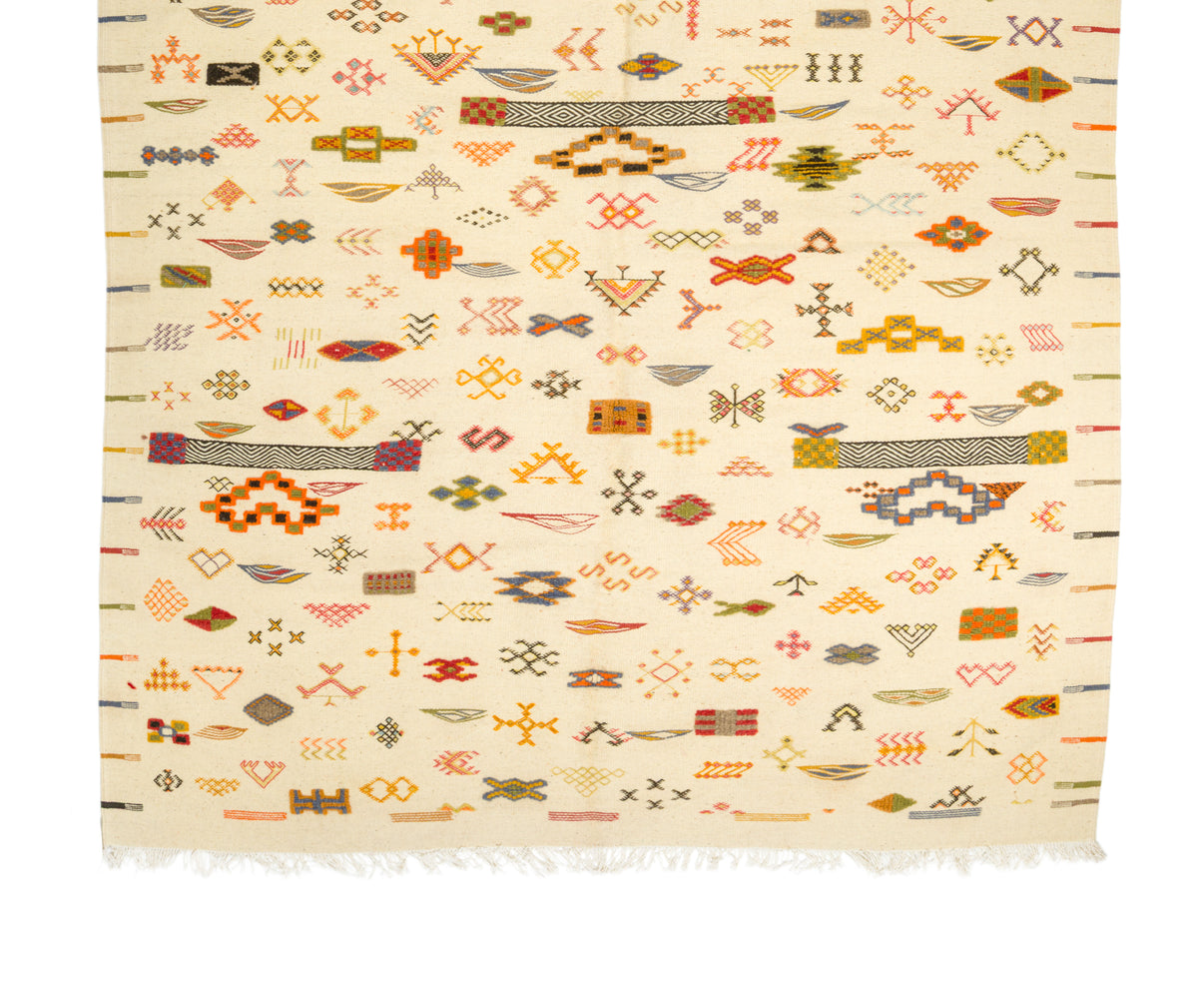 A square cream-colored woven rug with a dense, colorful geometric pattern in orange, brown, red, and green, finished with white fringe on the bottom edge.