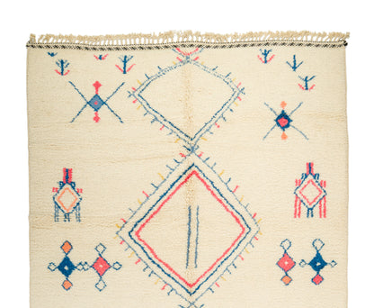 A square cream-colored Moroccan wool rug with a colorful geometric pattern in blue, red, and orange, featuring a central diamond motif and fringed top edge.