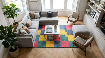 A colorful geometric patchwork area rug in red, yellow, green, and blue set in a stylish living room featuring a large gray sectional sofa, , a white coffee table, and light wood flooring.