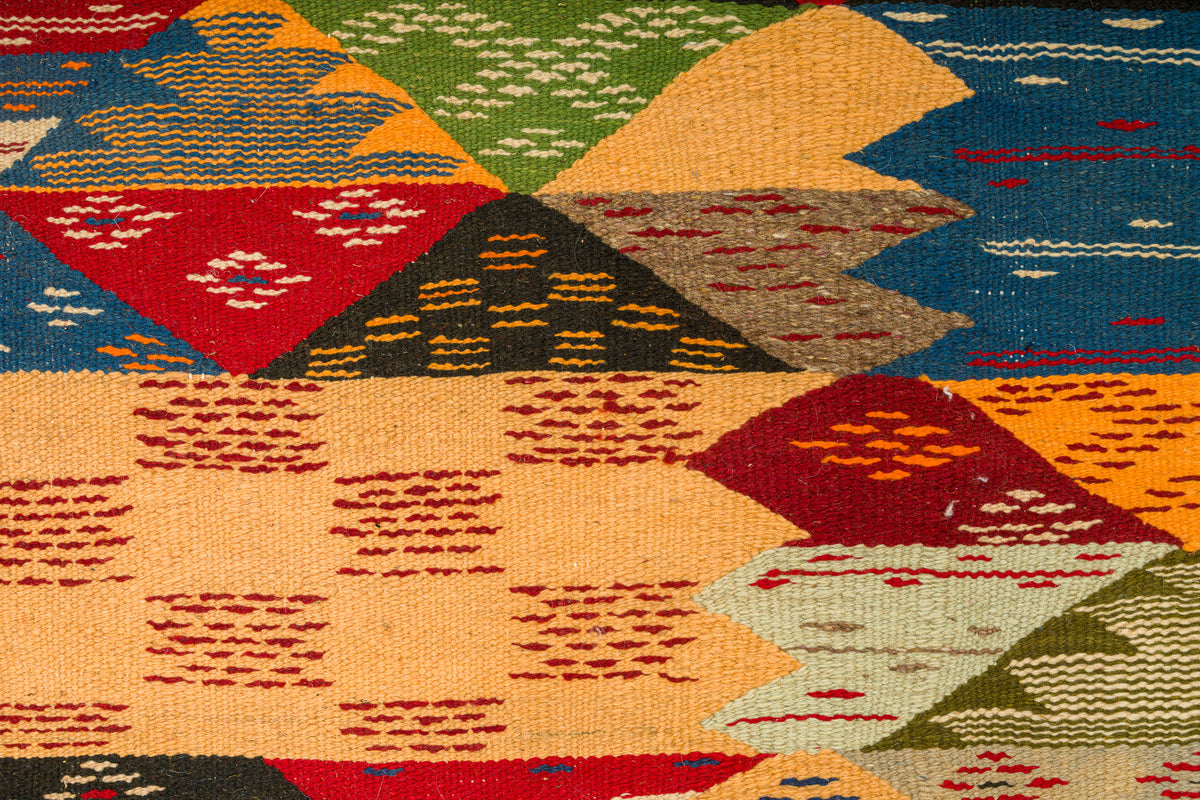 A close-up of a woven moroccan rug with a geometric cubism design in multiple colors including red, blue, green, orange, beige, and black.