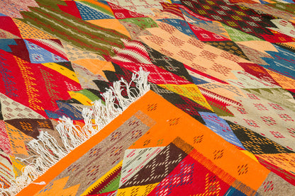 A close-up of a colorful  cubist moroccan rug with white fringe, showing a variety of geometric patterns and bright colors including orange, red, blue, green, and beige.