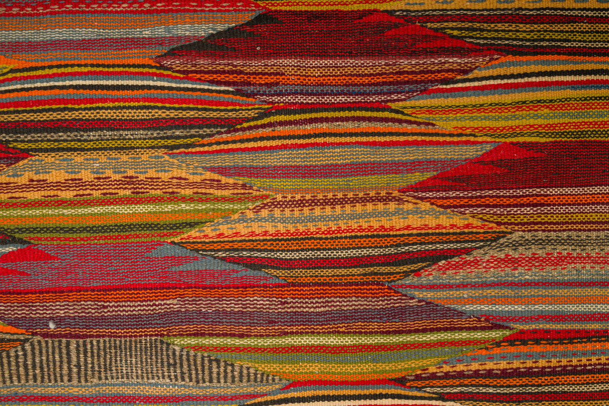A close-up of a moroccan taznakht rug with a multicolor cubist pattern of layered hills and stripes in red, orange, yellow, green, brown, and blue.