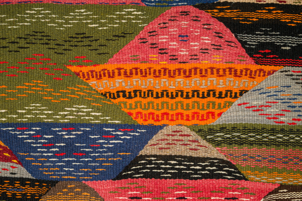 A close-up of a handwoven moroccan rug from Taznakht with a geometric patchwork design in multiple colors, including pink, orange, blue, green, black, and beige.