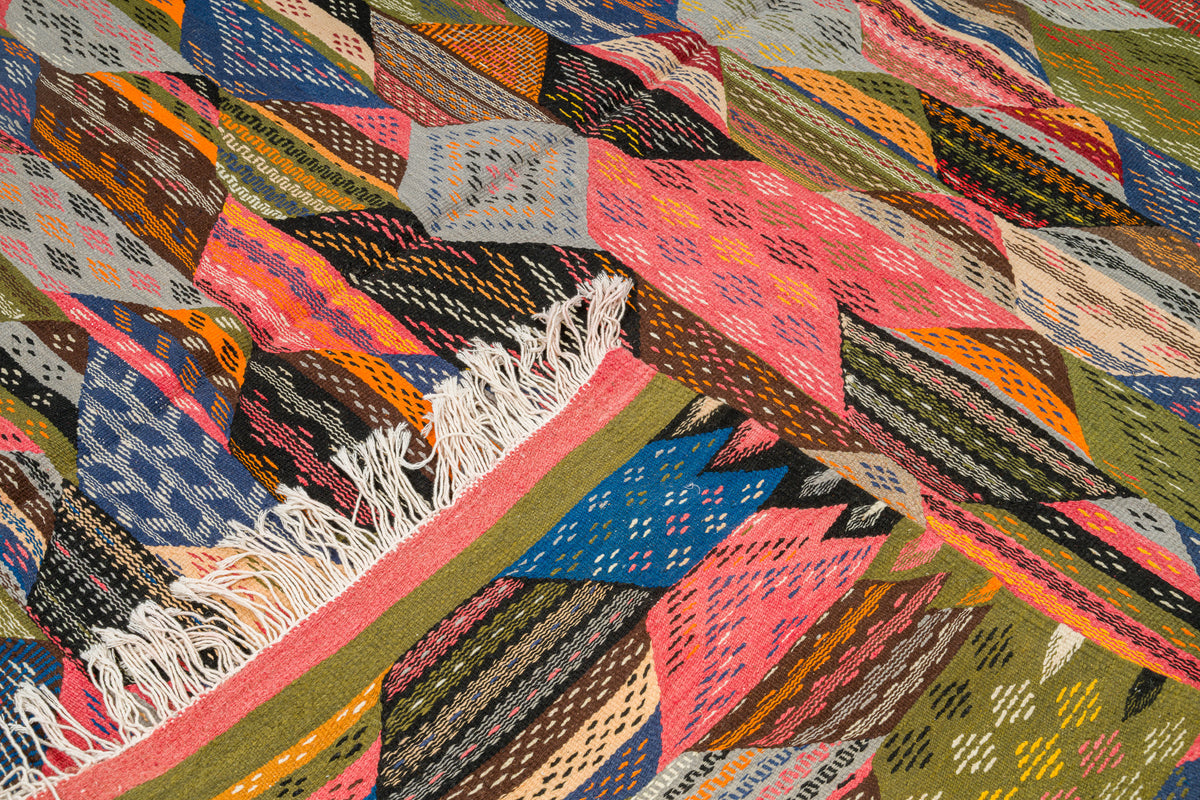 A close-up of a handwoven moroccan rug from Taznakht with a multicolor geometric cubist pattern and white fringe along one edge.