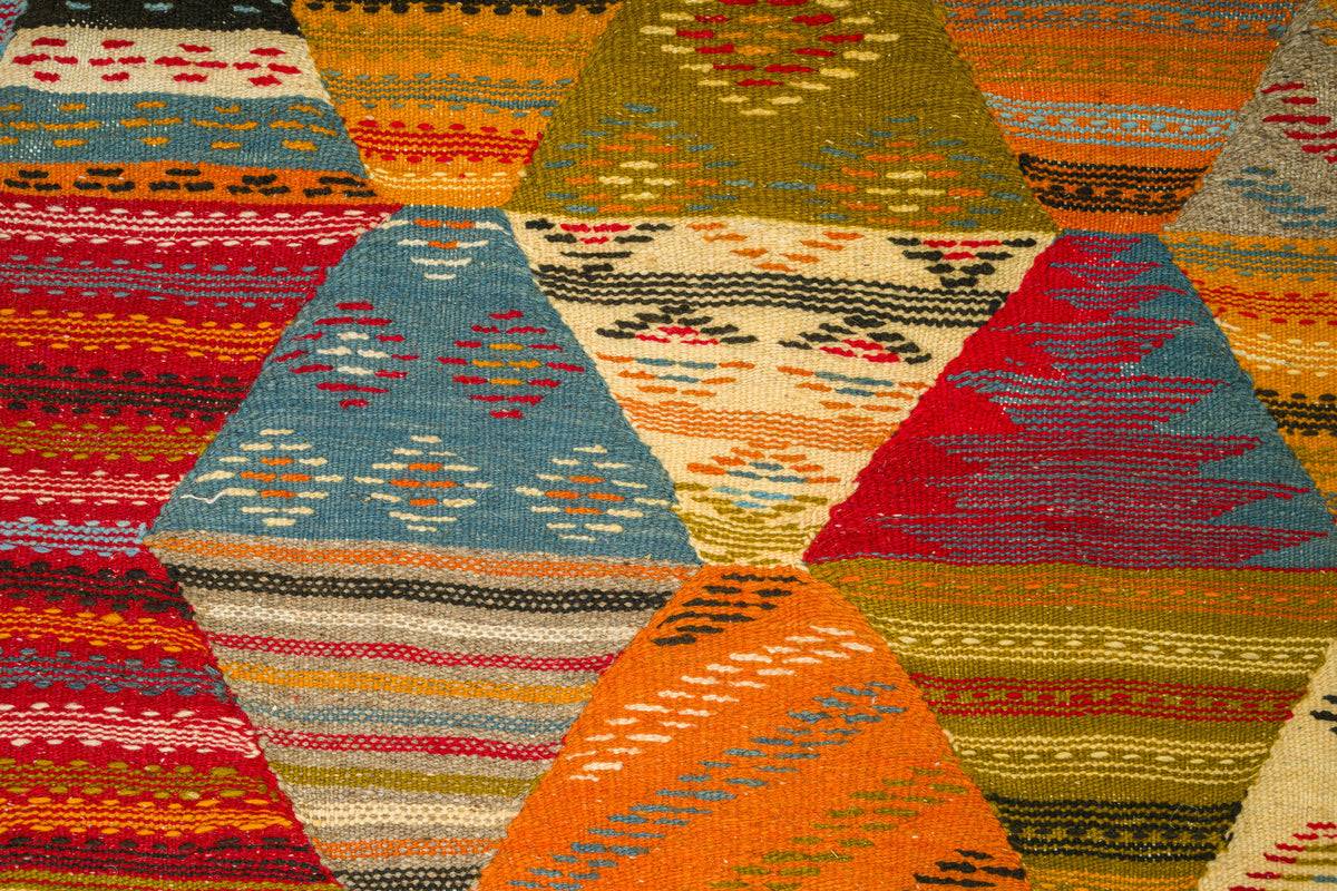A close-up of a woven moroccan rug  with a geometric cubist design in multiple colors, including orange, red, blue, beige, olive green, and black.
