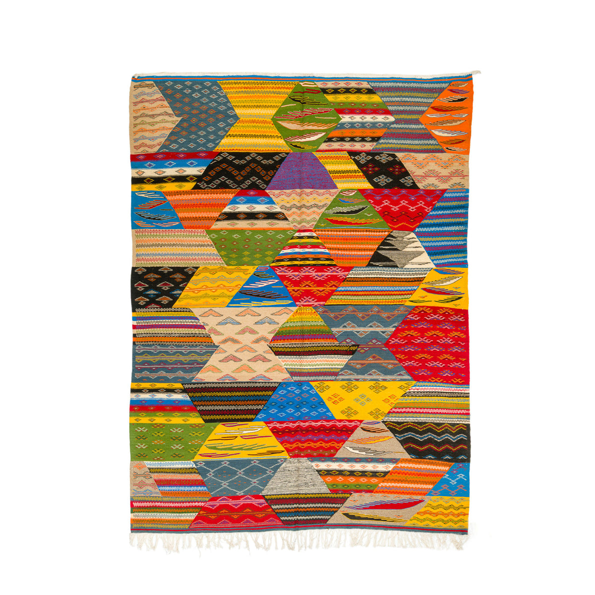 A colorful geometric patterned moroccan rug from taznakht with a patchwork cubist design of hexagons and triangles in multiple vibrant colors, finished with white fringe at the bottom, shown flat against a white background.