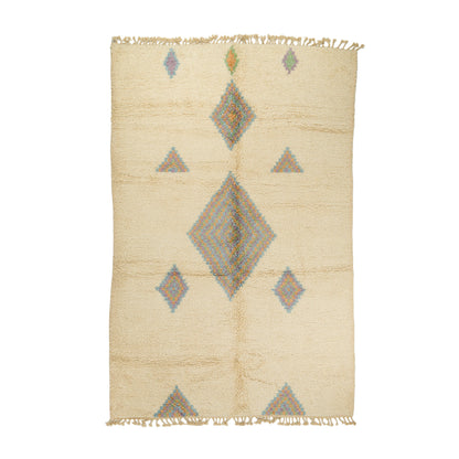 A rectangular woven rug with a cream-colored base and a geometric pattern featuring a large central diamond, smaller diamonds, and triangles in muted blue, gray, and orange accents. The rug has fringed edges on all sides and is photographed flat against a solid white background.