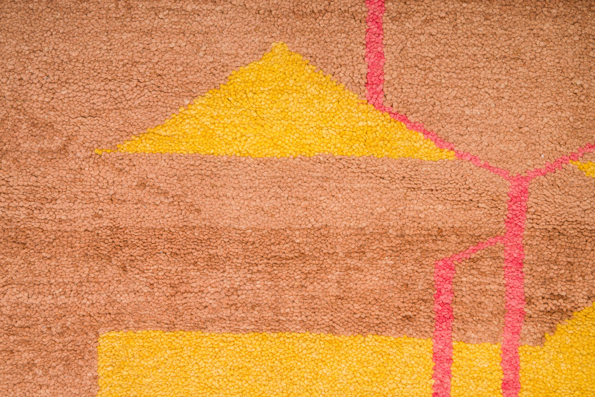 A close-up a moroccan high pile rug featuring a geometric pattern with a warm brown base, bright yellow triangular and rectangular shapes, and pink linear accents.