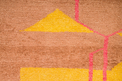 A close-up a moroccan high pile rug featuring a geometric pattern with a warm brown base, bright yellow triangular and rectangular shapes, and pink linear accents.