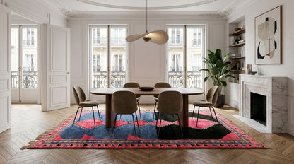 A large, colorful area rug with a red, blue, and black geometric pattern is styled in a bright, classic Parisian dining room with a wooden dining table and chairs.