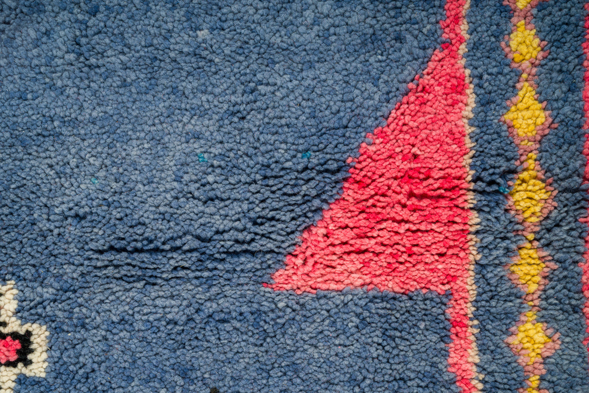 Close-up of a moroccan wool rug featuring a deep blue field with a prominent red geometric motif and yellow diamond accents.