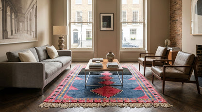 A Moroccan Azilal rug.
A styled living room featuring a prominent blue and red patterned area rug under a glass-top coffee table, flanked by a gray sofa and two brown leather armchairs.