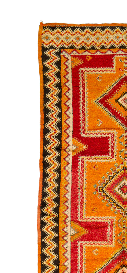 A close-up of a patterned textile or rug corner showing bold geometric stripes in orange, red, black, and cream on a white background.