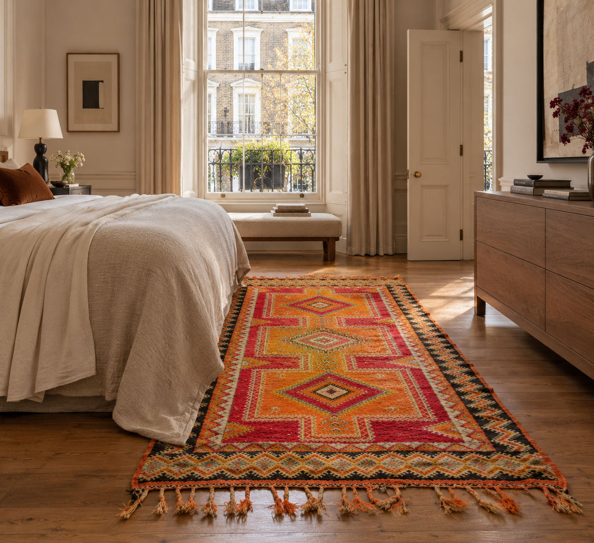 A colorful geometric area rug with tassels laid out on a wooden floor in a bright, modern bedroom setting.