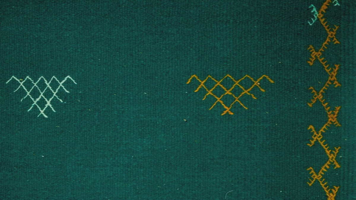 video close-up of a green moroccan rug handwoven with hand embroidered tribal motifs