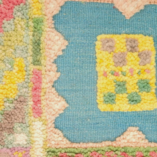 Close-up video of a colorful hand-knotted hand woven moroccan rug showing a blue central motif with a yellow floral center, surrounded by pink, green, and beige textured sections.