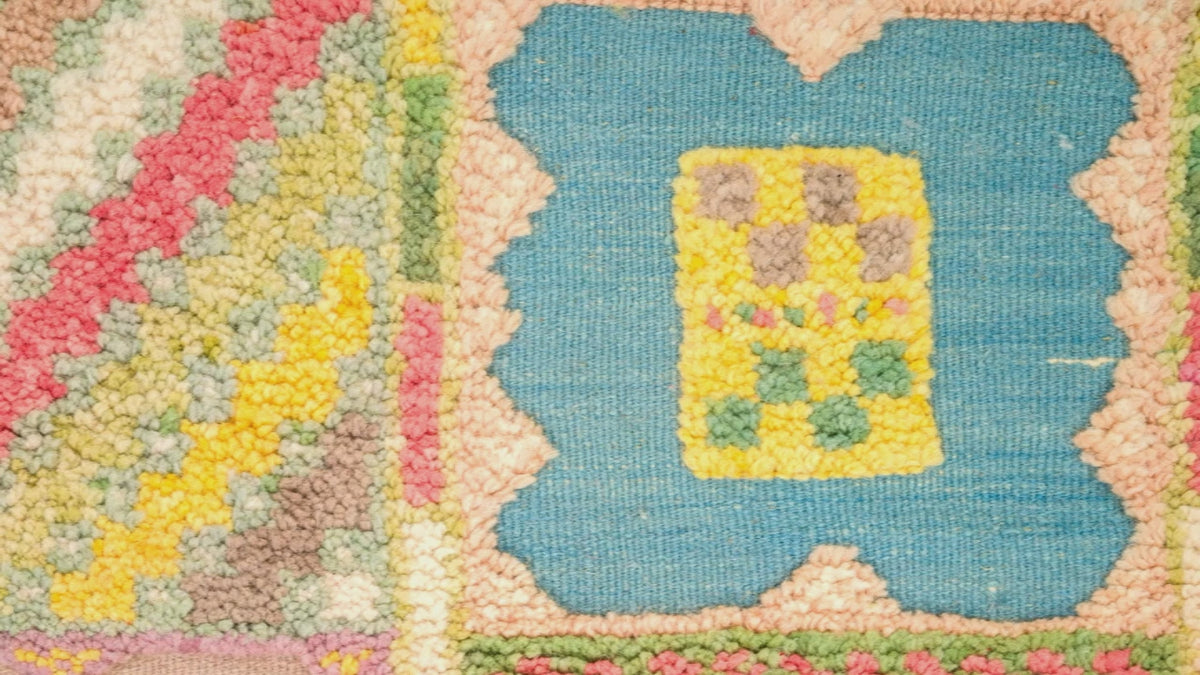 Close-up video of a colorful hand-knotted hand woven moroccan rug showing a blue central motif with a yellow floral center, surrounded by pink, green, and beige textured sections.